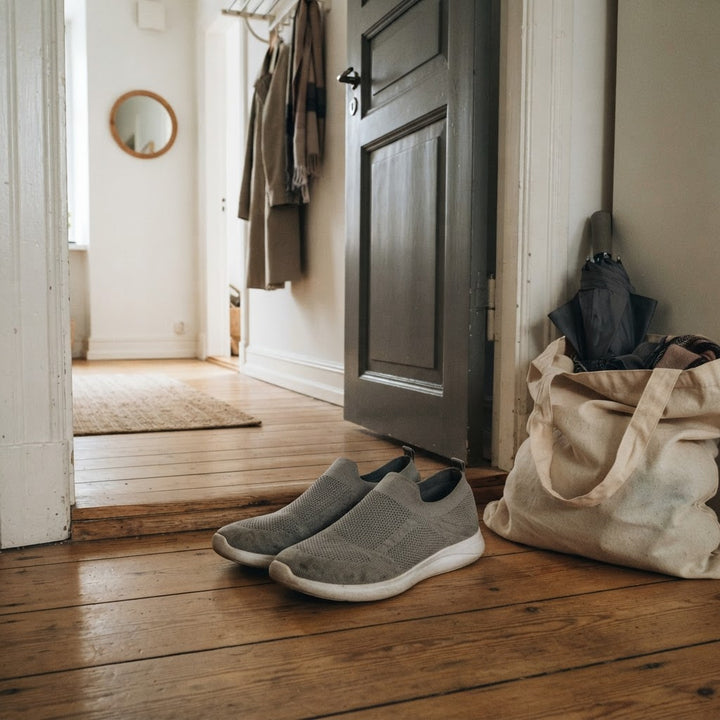 Grå stickade slip-on-skor i en hall bredvid en tygkasse